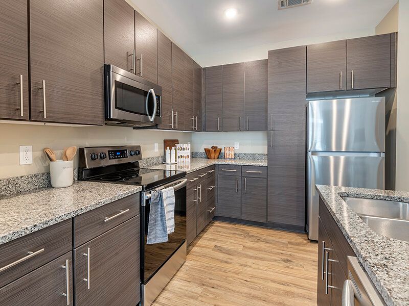Modern kitchen with gray cabinets, granite countertops, stainless steel appliances, and a double sink.