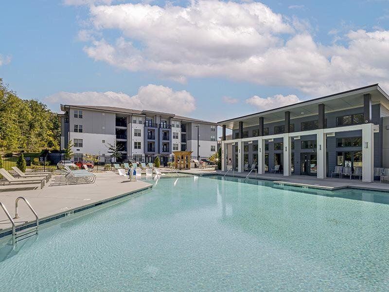 Outdoor apartment community pool with lounge chairs and a modern clubhouse.