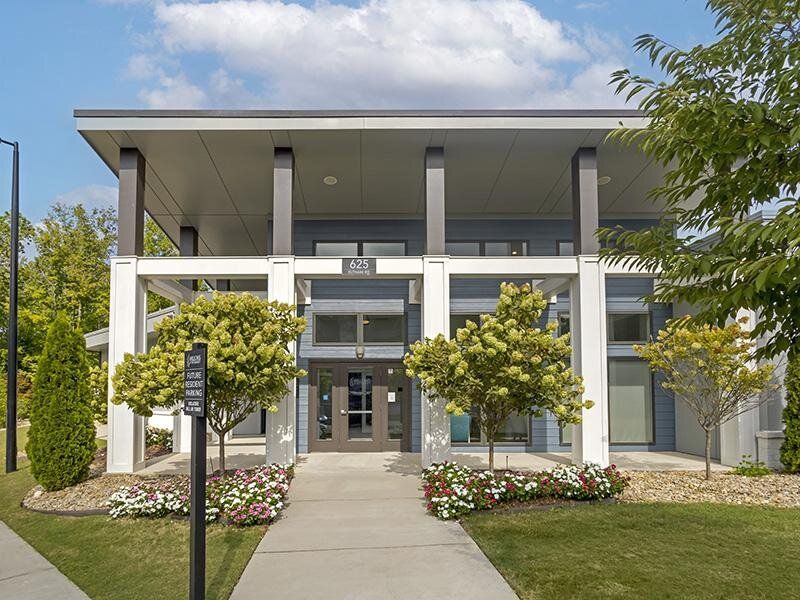 Exterior view of a modern apartment community entrance with glass doors and landscaped walkway.