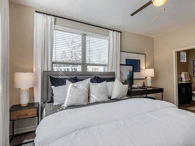 Bedroom in an apartment with a large bed, white bedding, multiple pillows, and two nightstands beside a window.