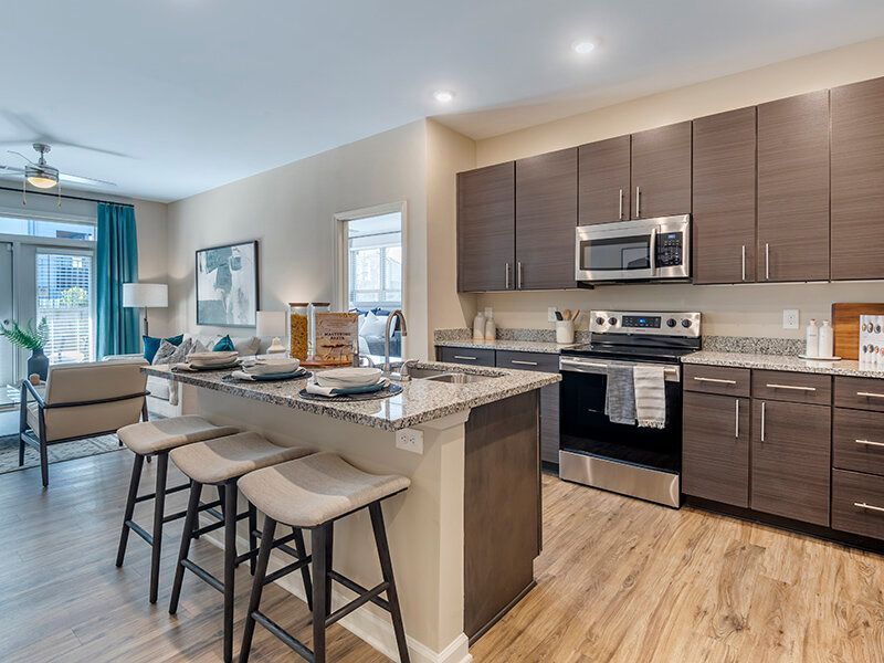 Modern kitchen with granite island, dark wood cabinets, and stainless-steel appliances in an open living area.