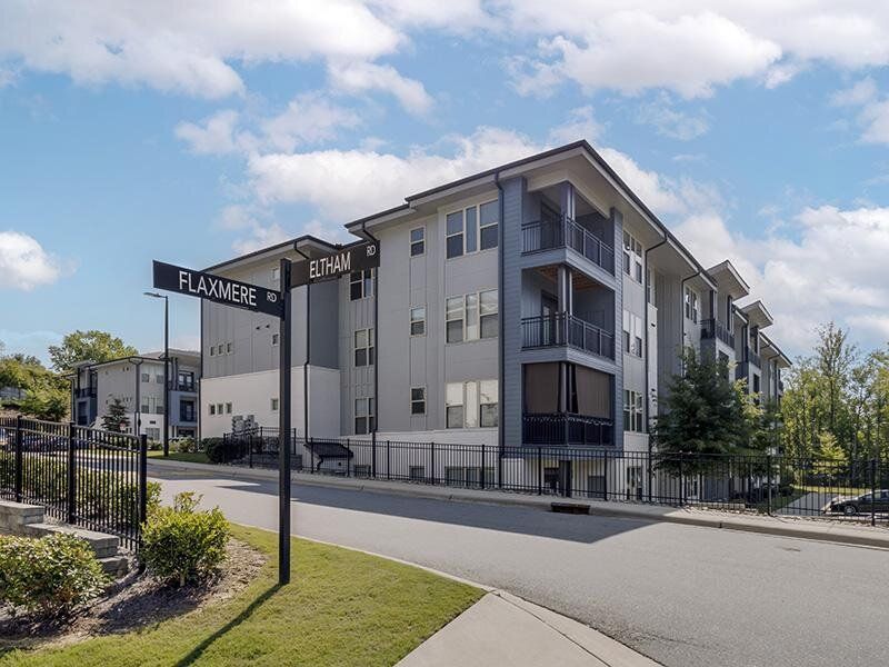 Exterior view of a modern apartment building with a gated entry and street sign poles.