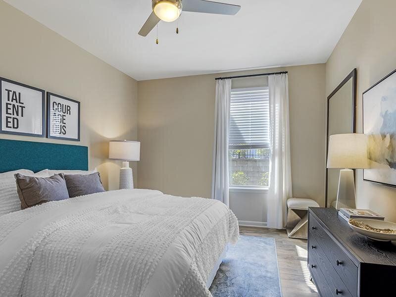 Bedroom with white bedding, two nightstands, dresser, and window with sheer curtains.