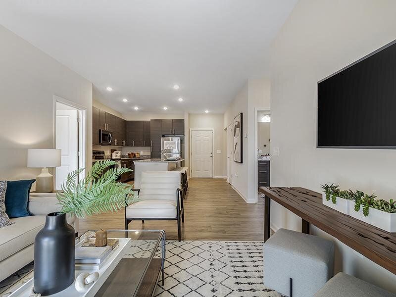Open-concept living area with sofa, chairs, coffee table, and a modern kitchen in the background.
