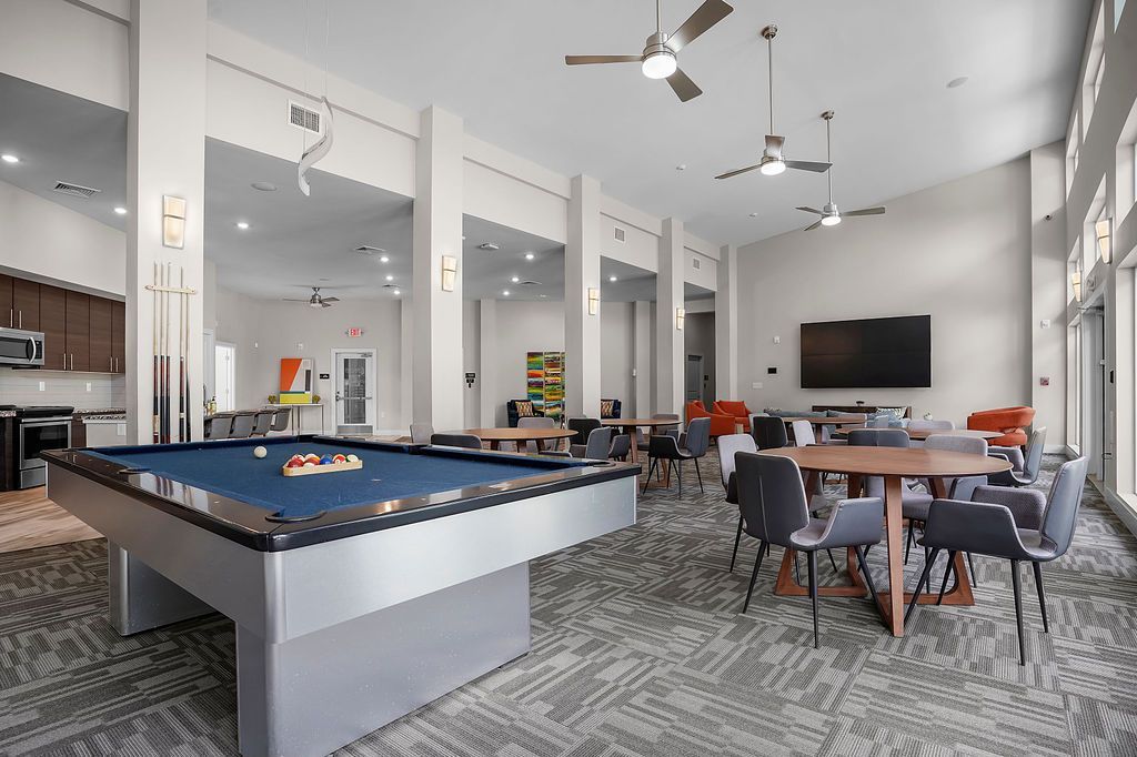 Open modern community lounge with a pool table, kitchenette, and seating areas.