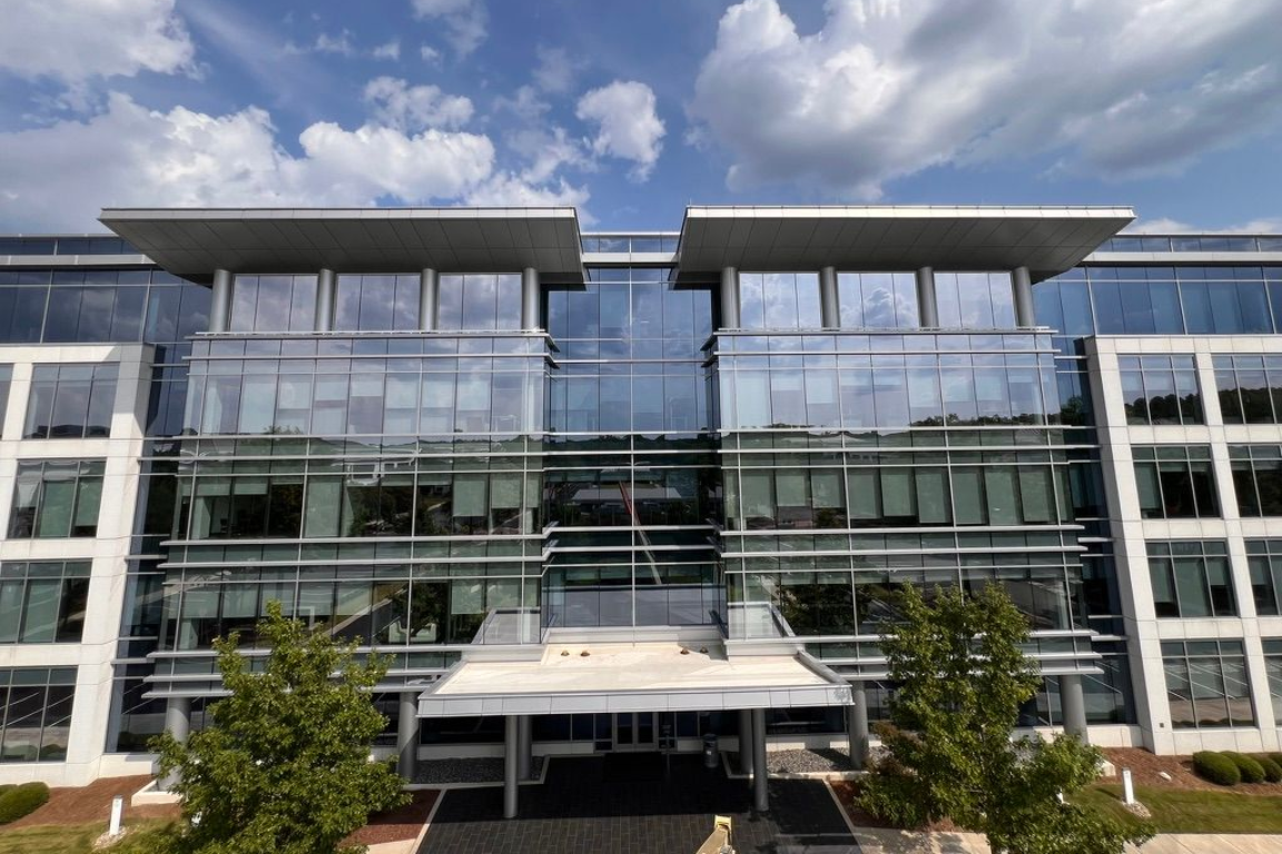 Modern glass office building with blue sky and clouds.