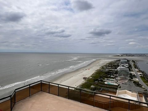 Overlooking a beach, sea, and land from a high-rise balcony under a cloudy sky.