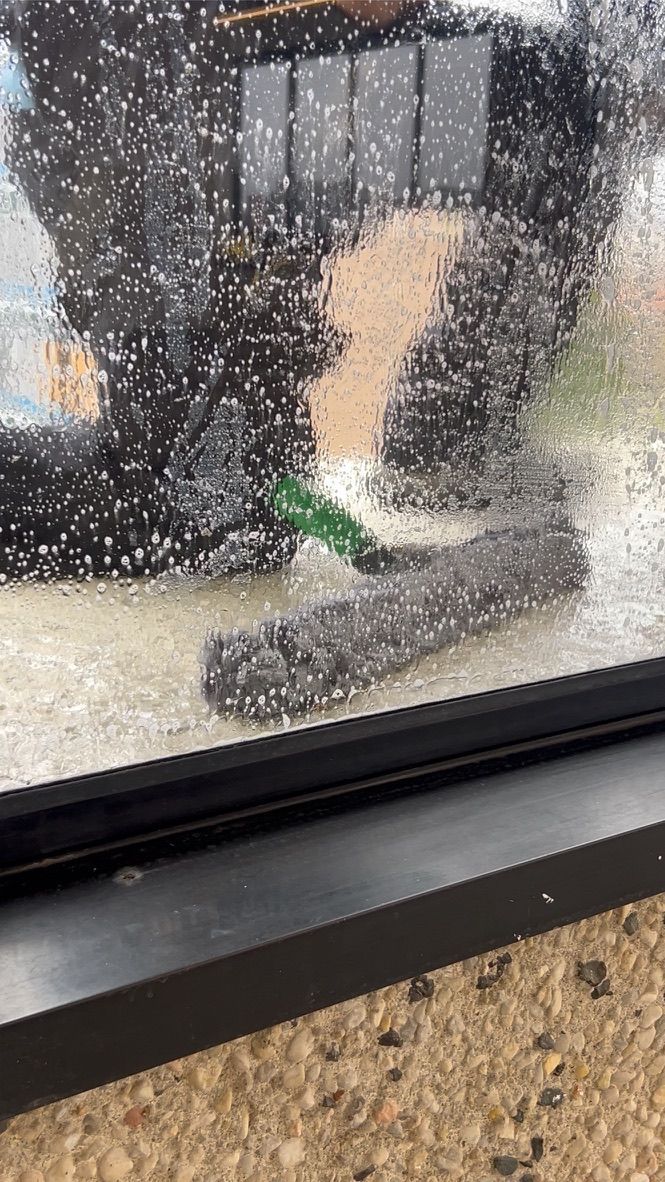 A blurry view through a wet window. A long, grey object lies near a grassy area.