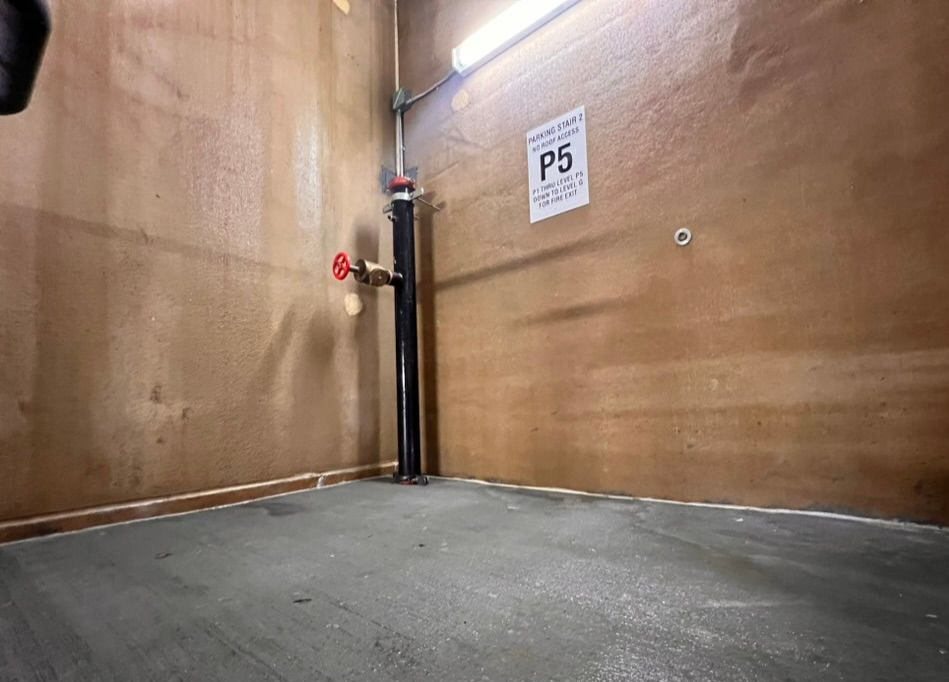 A small storage room with a pipe and valve against a wooden wall; sign reads P5.