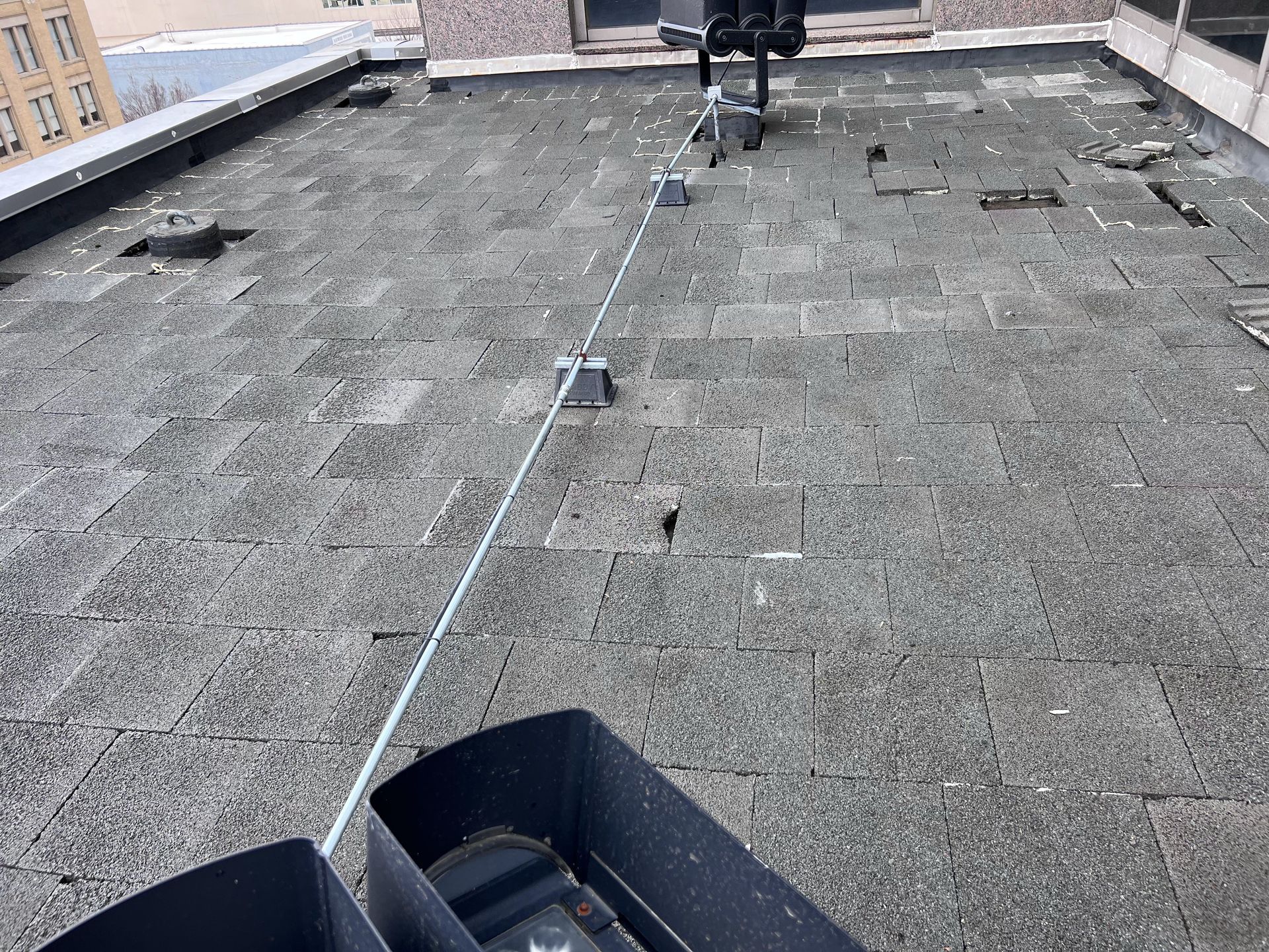 Rooftop with safety cable system. Dark roof tiles, black bins in foreground. Cable stretches across.
