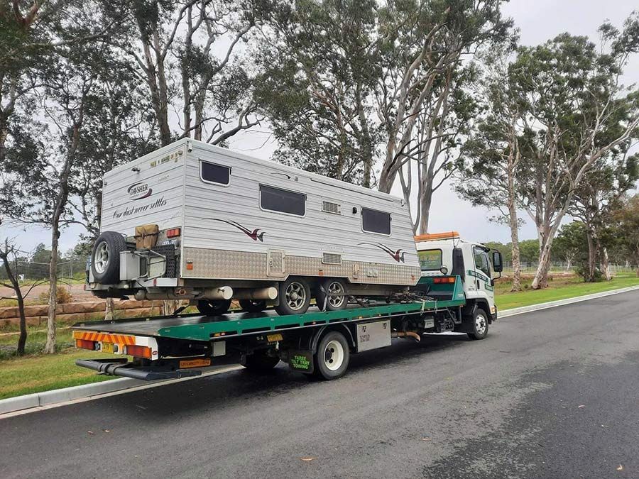 A Tow Truck Is Carrying A Row Of Cars On A Flatbed Trailer — Taree Tilt Tray Towing In Hallidays Point, NSW