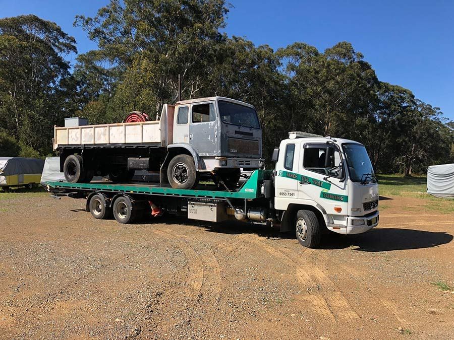 A Tow Truck is Towing a Dump Truck in a Gravel Lot — Taree Tilt Tray Towing In Harrington, NSW