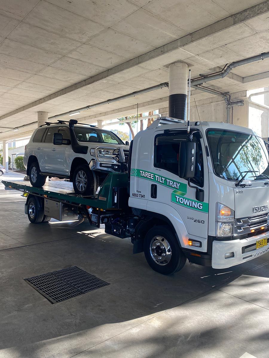 A Tow Truck Is Towing A White SUV In A Parking Garage — Taree Tilt Tray Towing In Taree, NSW