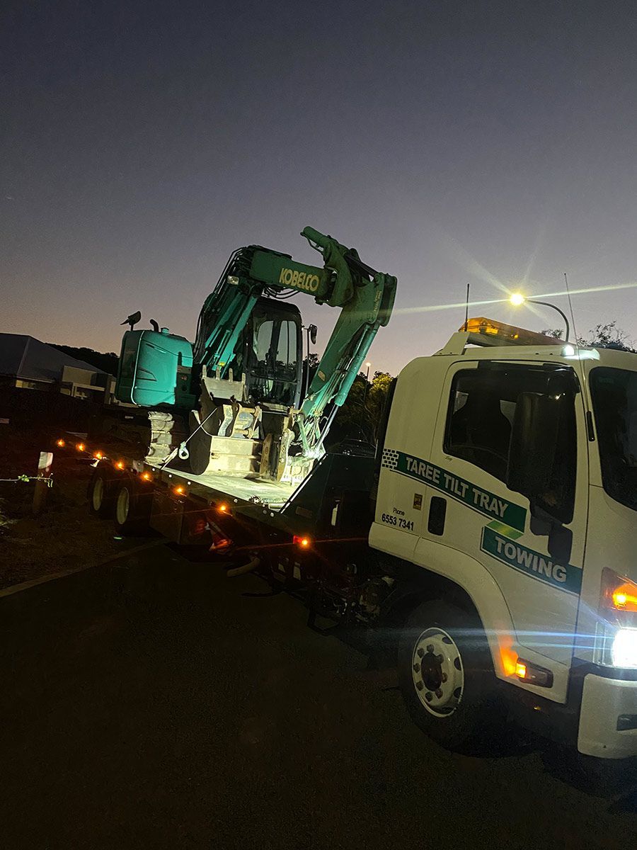 A Tow Truck is Carrying a Green Excavator on the Back of It — Taree Tilt Tray Towing In Tuncurry, NSW