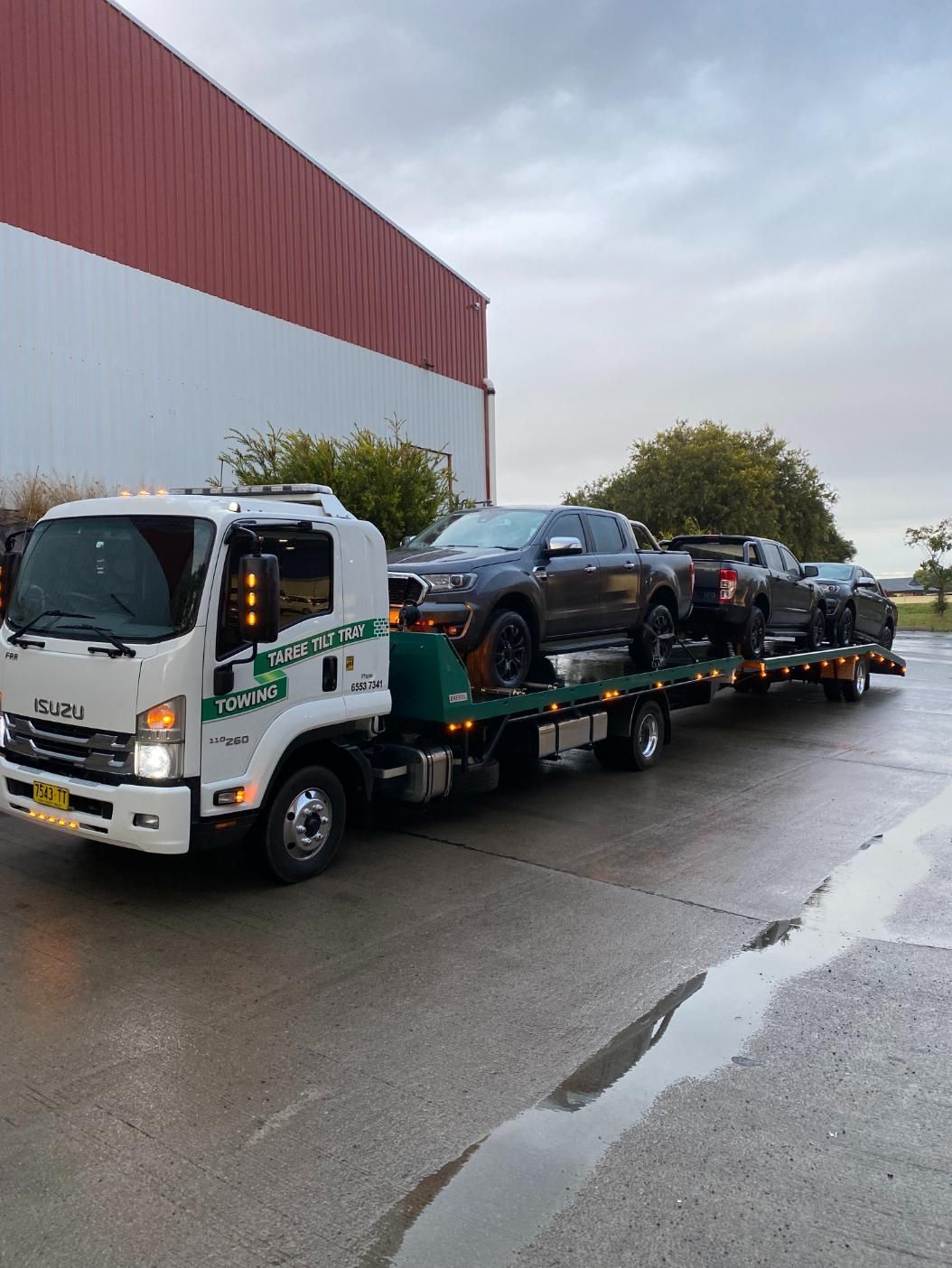 A Tow Truck Is Carrying A Bunch Of Cars On A Trailer — Taree Tilt Tray Towing In Pampoolah, NSW