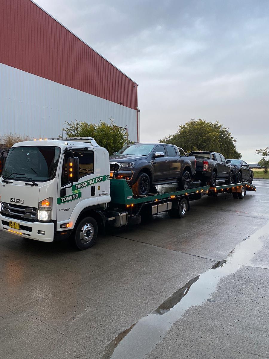 A Tow Truck Is Carrying A Row Of Cars On A Flatbed Trailer — Taree Tilt Tray Towing In Pampoolah, NSW