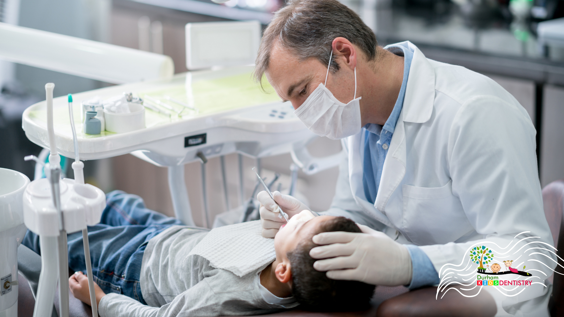 A dentist is examining a young boy 's teeth in a dental chair.