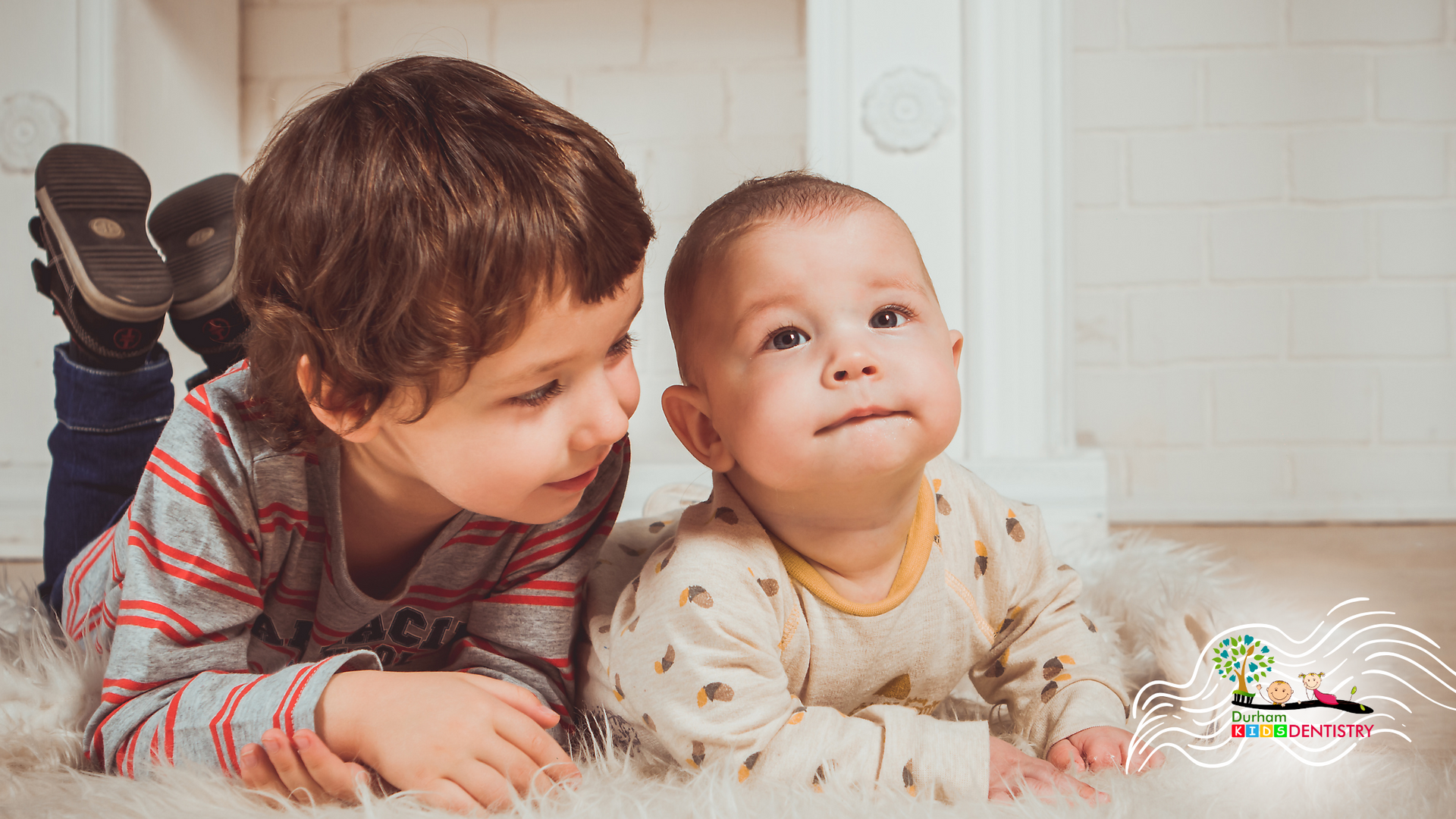 Two young boys are laying on the floor next to each other.