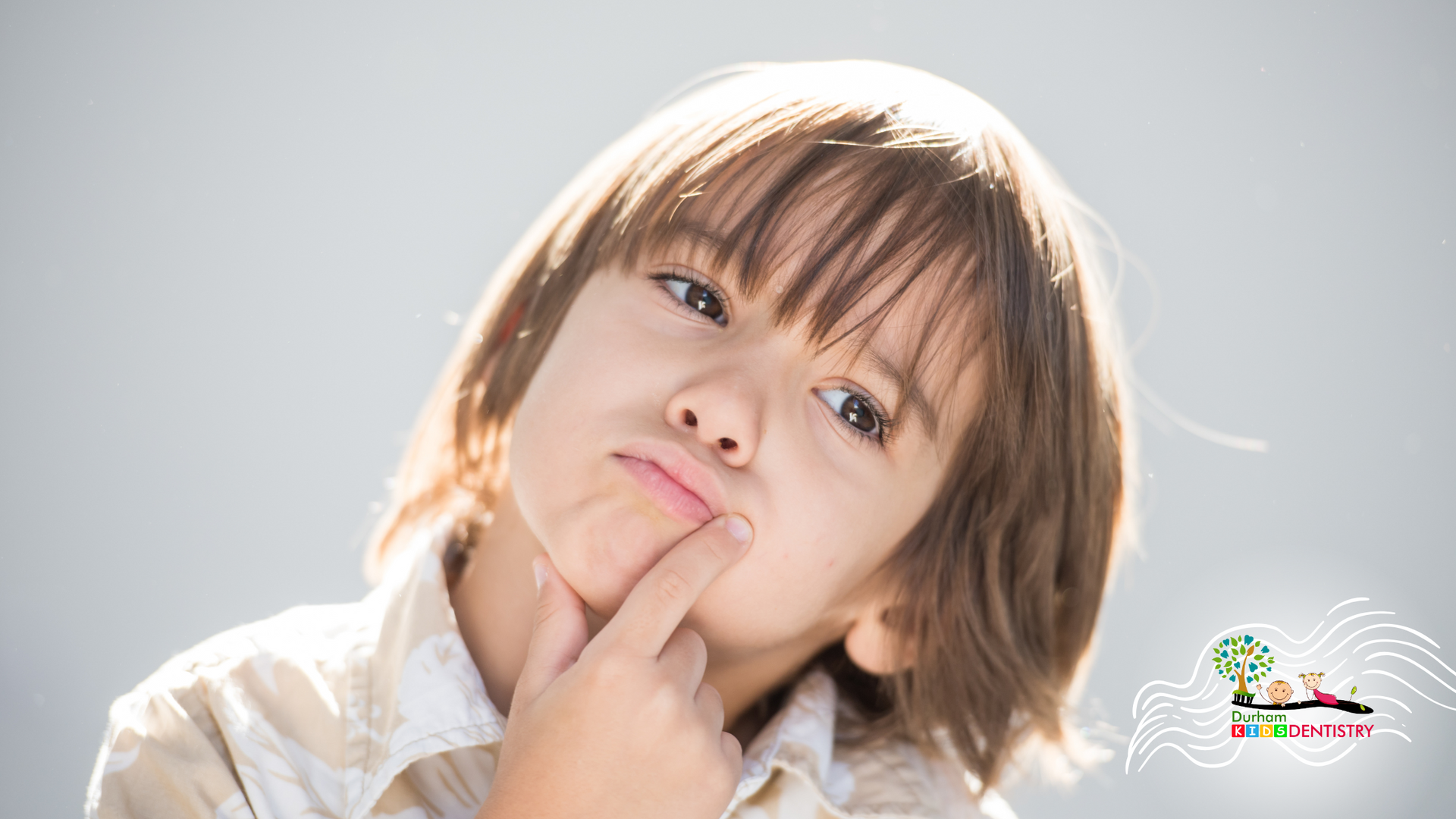 A young boy is making a funny face with his finger on his chin.