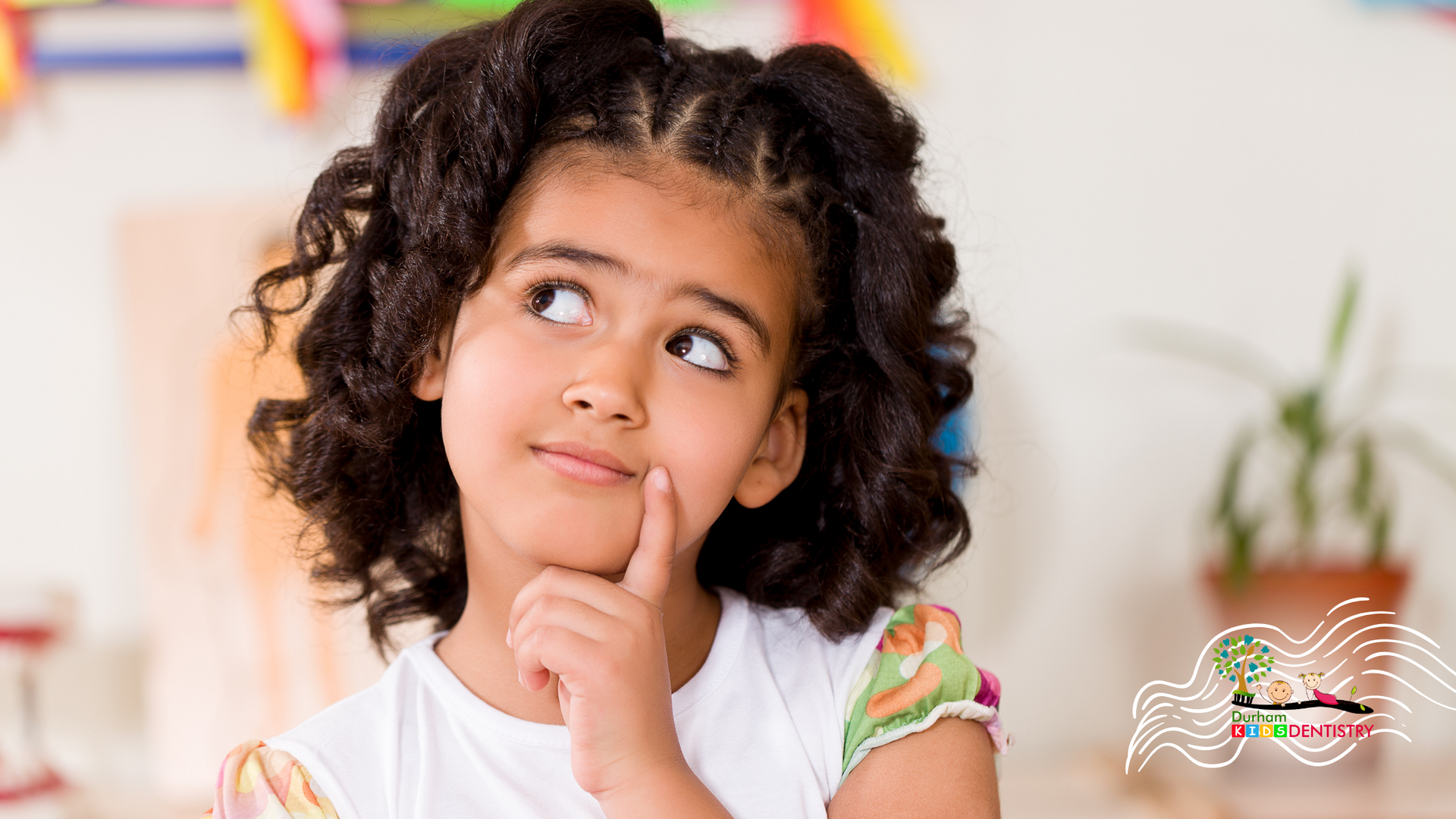 Girl with curly brown hair, looking upwards thoughtfully, finger on chin.