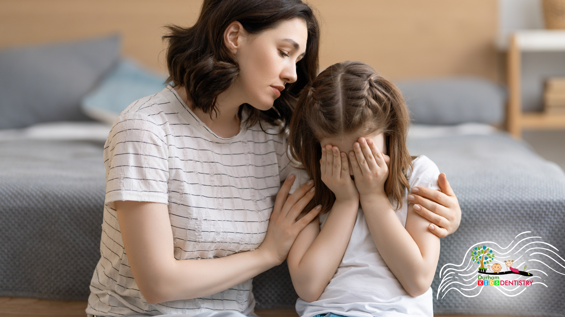 Woman comforts crying girl, hand on her shoulder, in a bedroom.