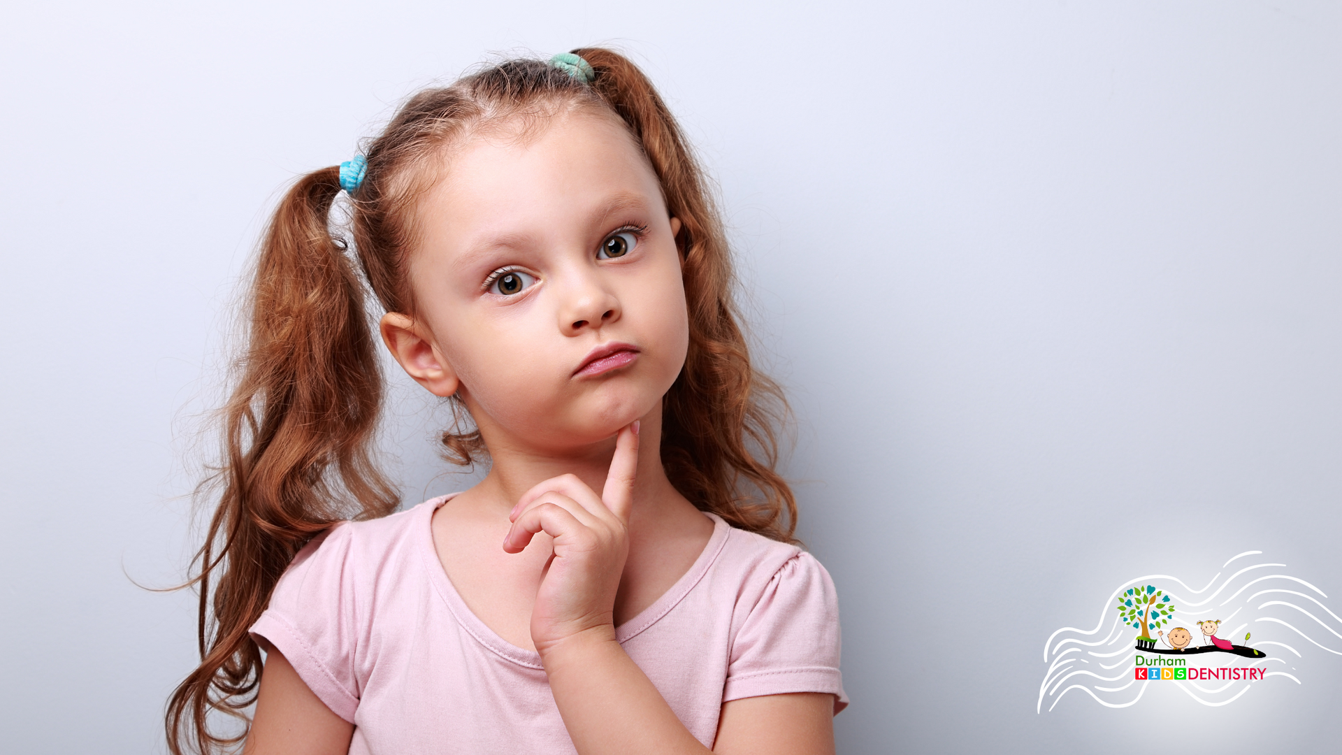 A little girl with pigtails is thinking with her hand on her chin.