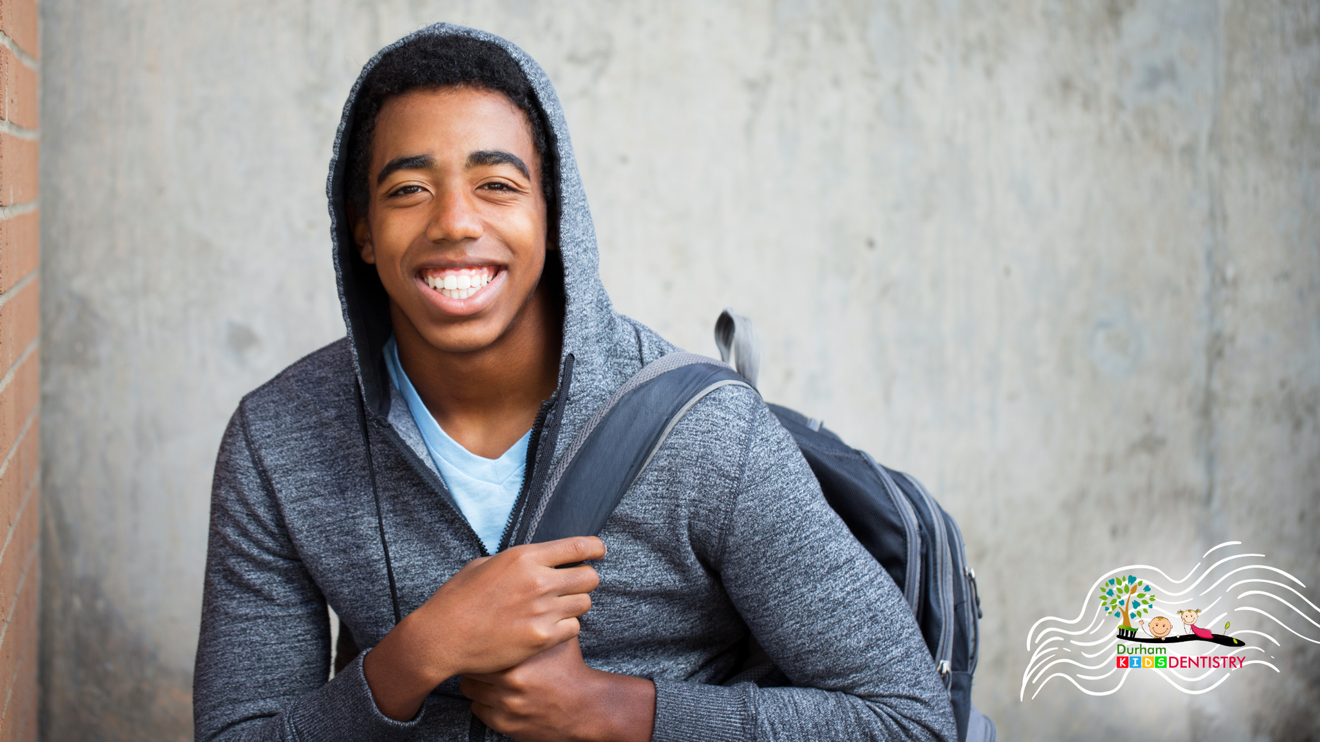 A young man wearing a hoodie and carrying a backpack is smiling.