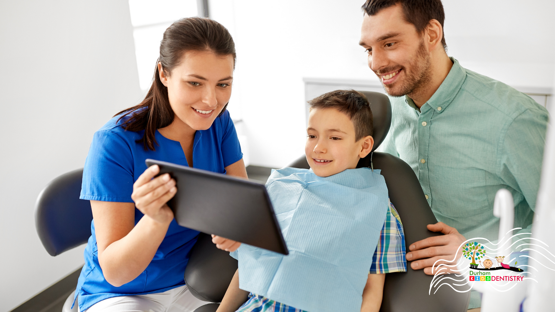 A man and a woman are looking at a tablet while a child is sitting in a dental chair.