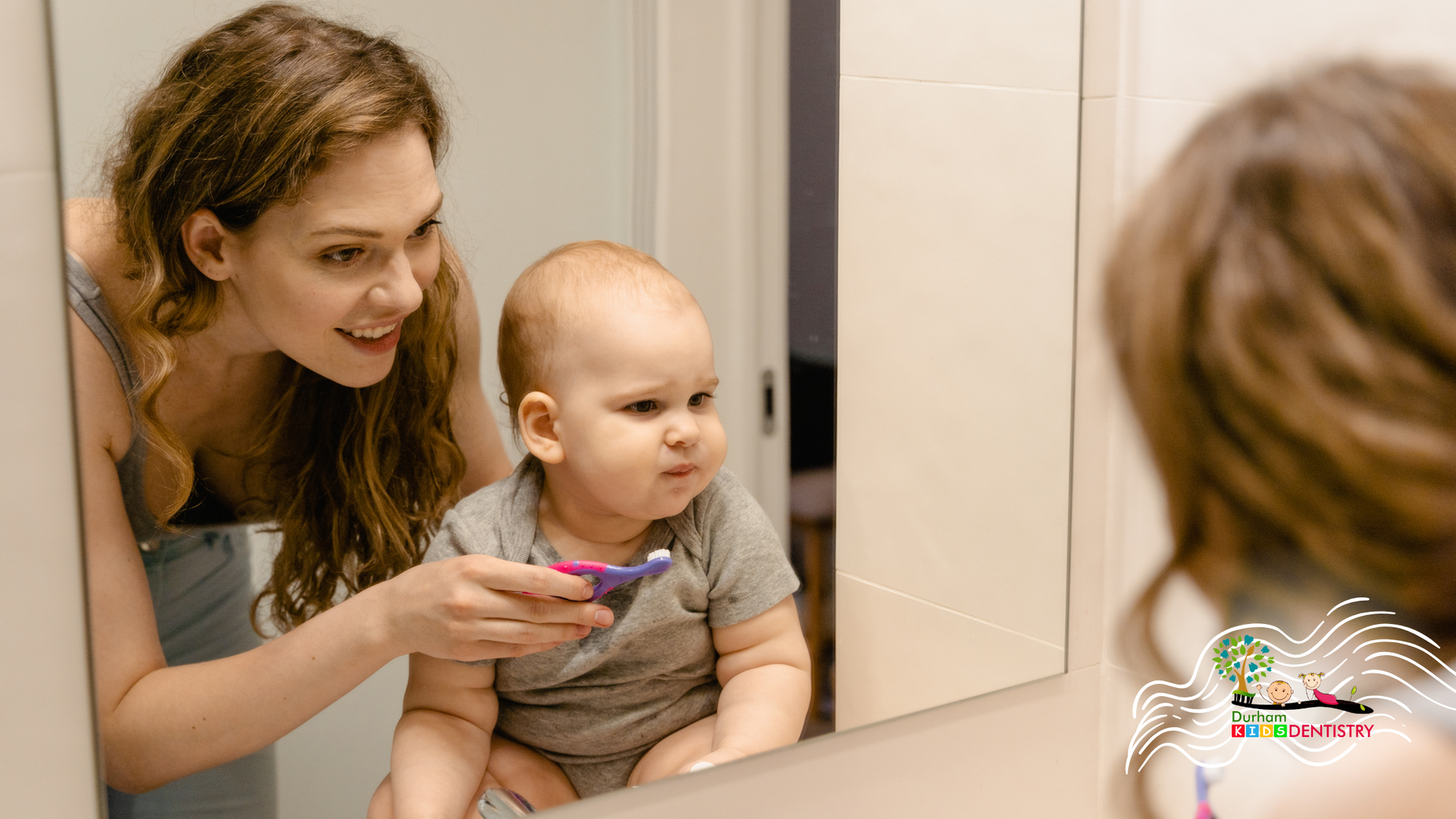 A woman is brushing her baby 's teeth in front of a mirror.