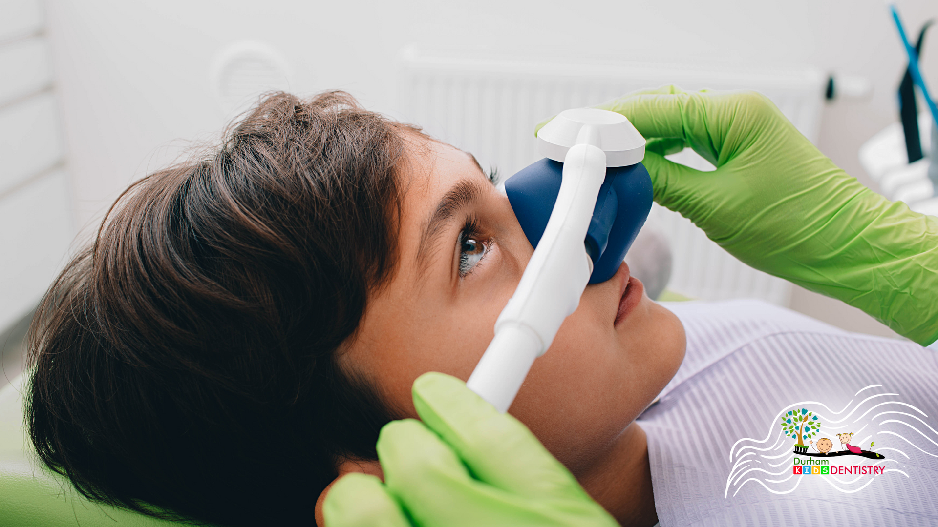 Boy receiving dental care, with an oxygen mask, held by gloved hands.
