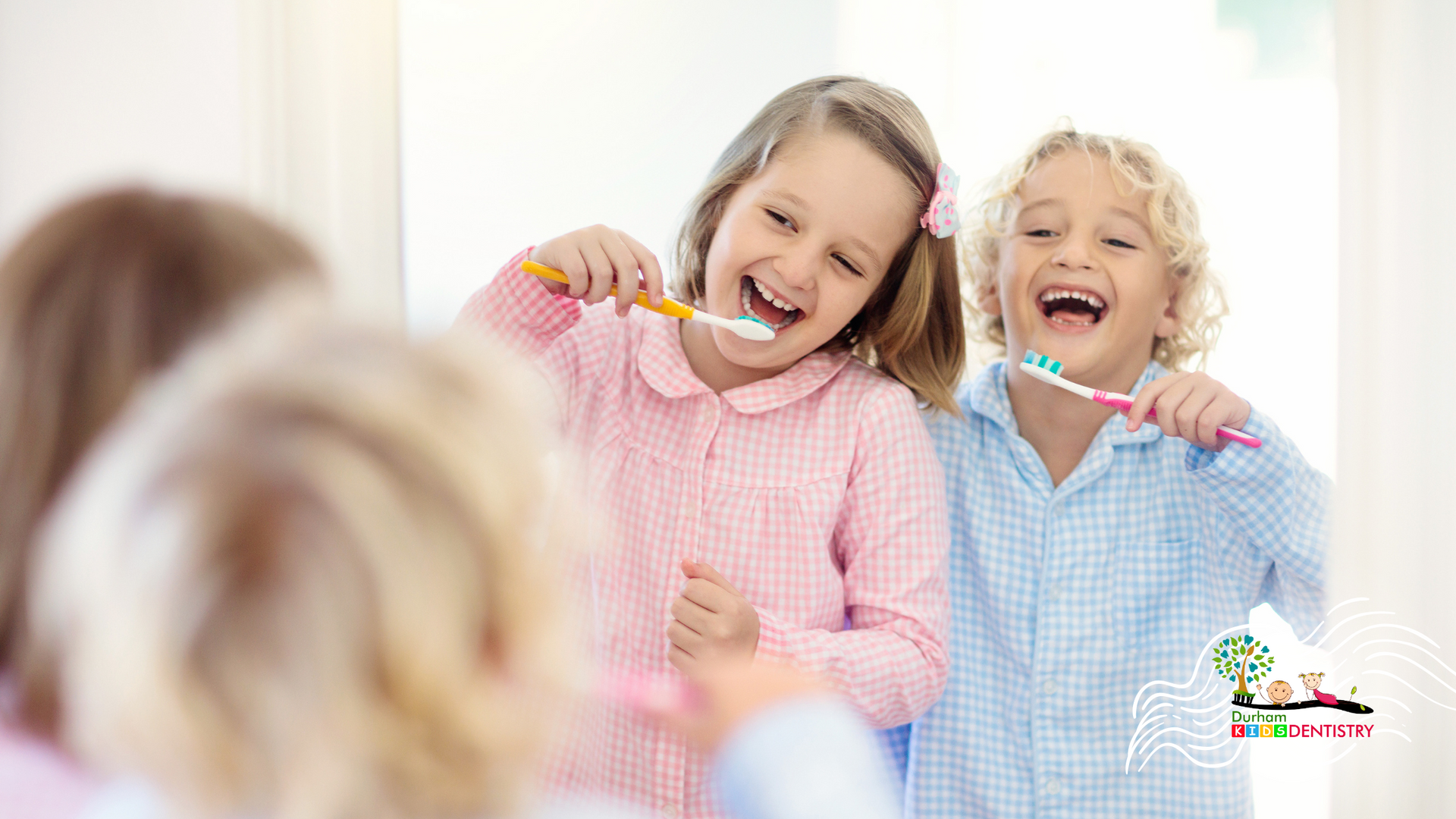 A boy and a girl are brushing their teeth in front of a mirror.