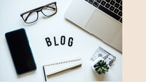 A flat-lay of a laptop, smartphone, glasses, notebook, pen, and a hundred-dollar bill with 