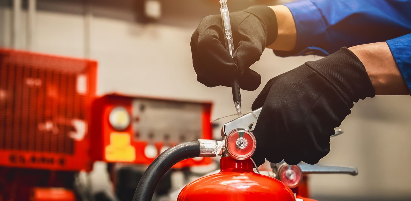 Persona con guantes negros inspeccionando un extintor rojo, probablemente para mantenimiento en un taller.