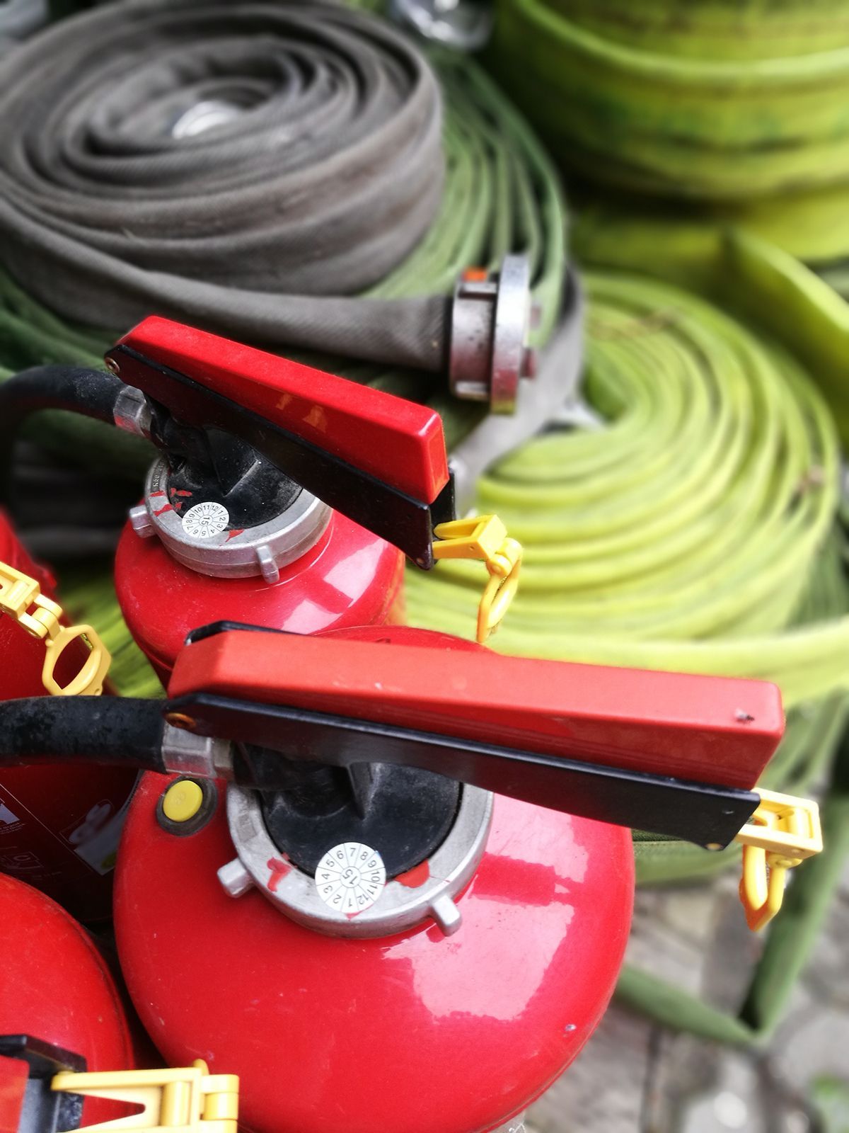 Extintores rojos con mangueras contra incendios enrolladas de color verde y gris en el fondo.