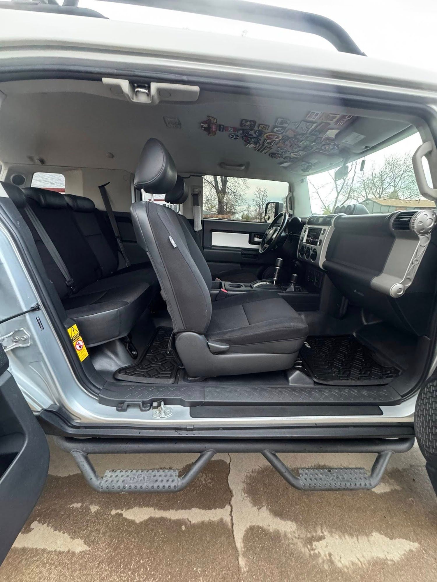 Interior of a silver Toyota FJ Cruiser with black seats, step bars, and patterned headliner, door open.
