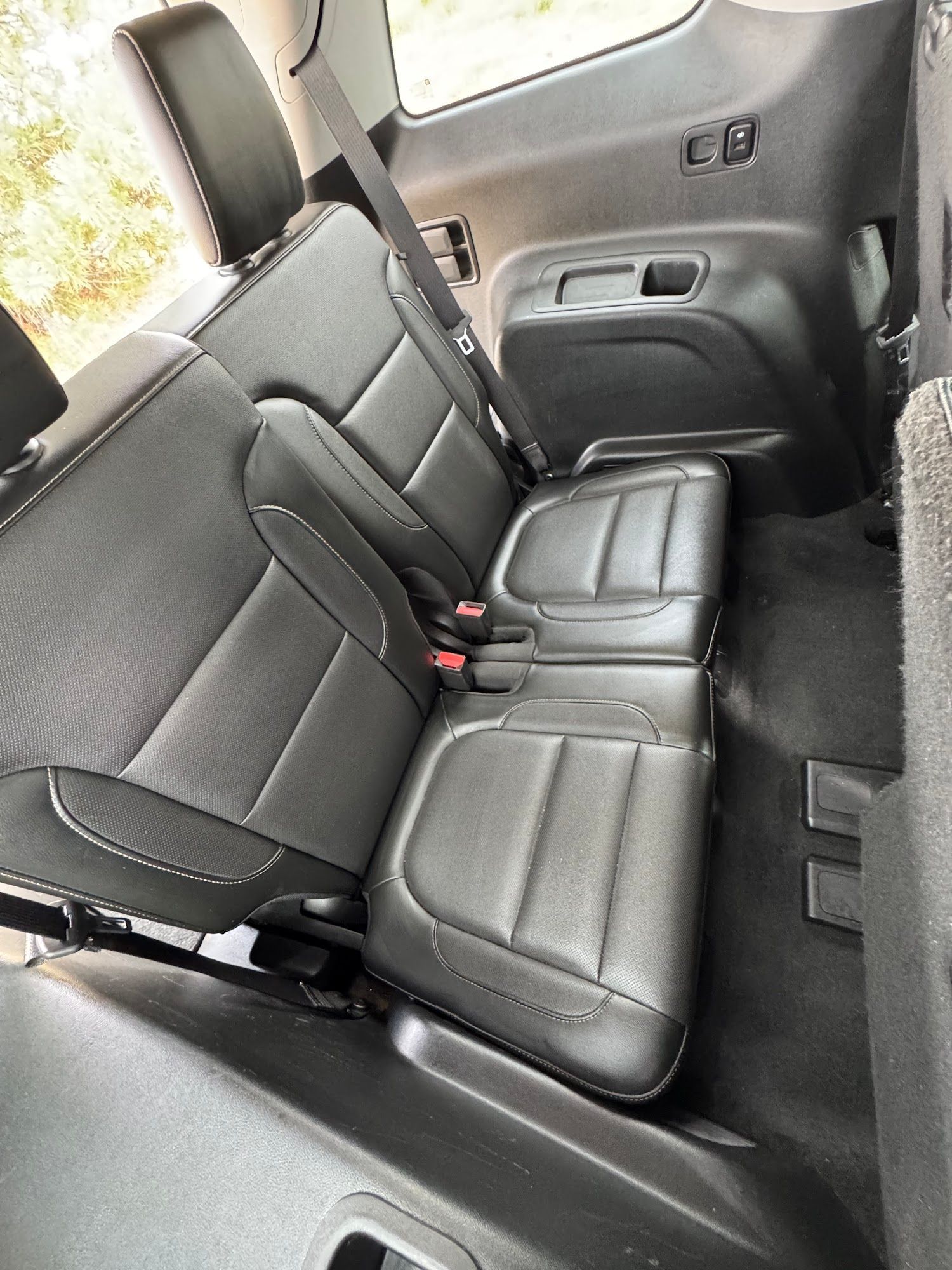 Black leather car seats in the second row, seatbelts visible, dark interior.