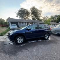Dark blue Honda CRV parked in front of a house, with a hose on the ground.