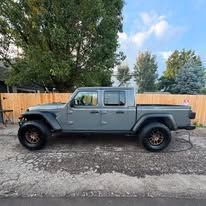 Gray Jeep truck parked on concrete near a wooden fence.