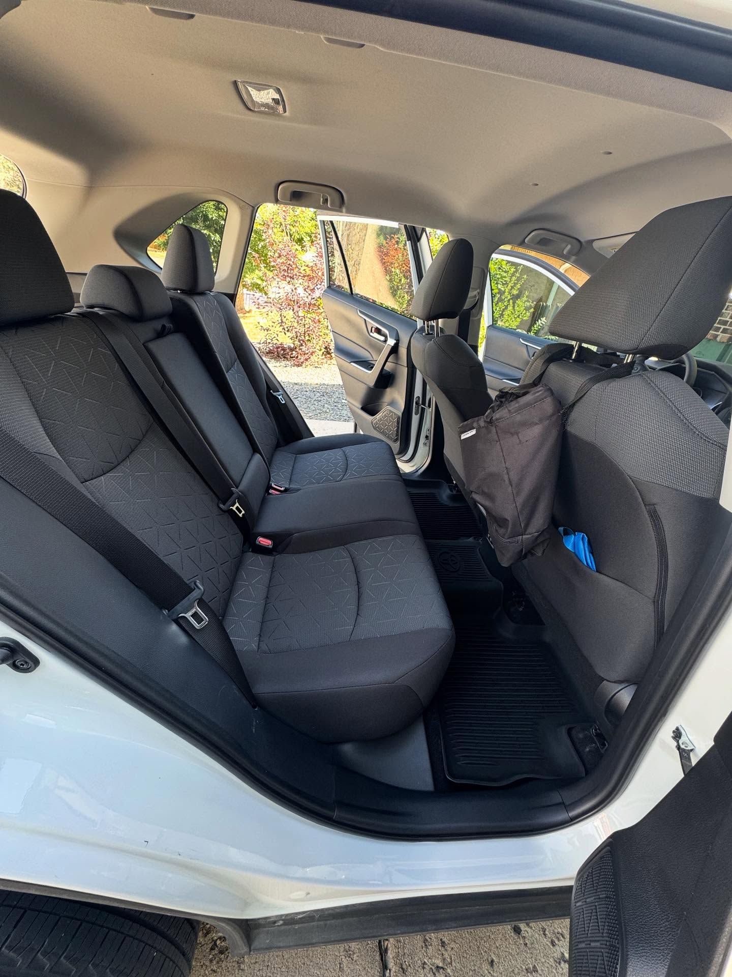 Interior view of a white car's back seat with black seats and floor mats. A black bag hangs from a seat.
