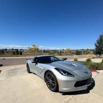 Silver sports car parked on pavement under blue sky.