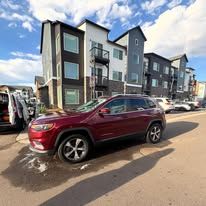 Red Jeep Cherokee parked in front of a modern apartment building on a sunny day.