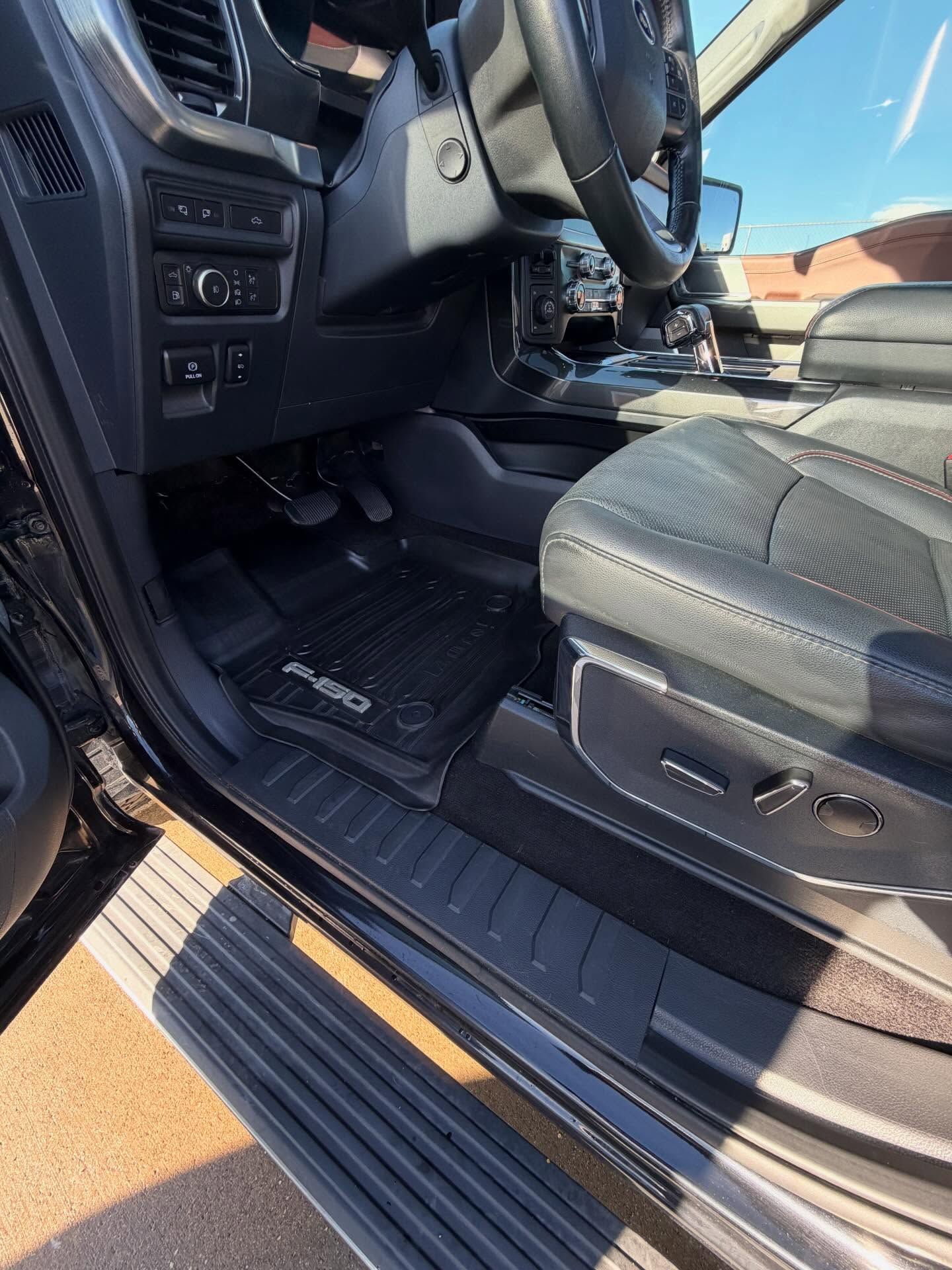 Interior of a black truck. Driver's side view. Shows floor mat, seat, pedals, and steering wheel.