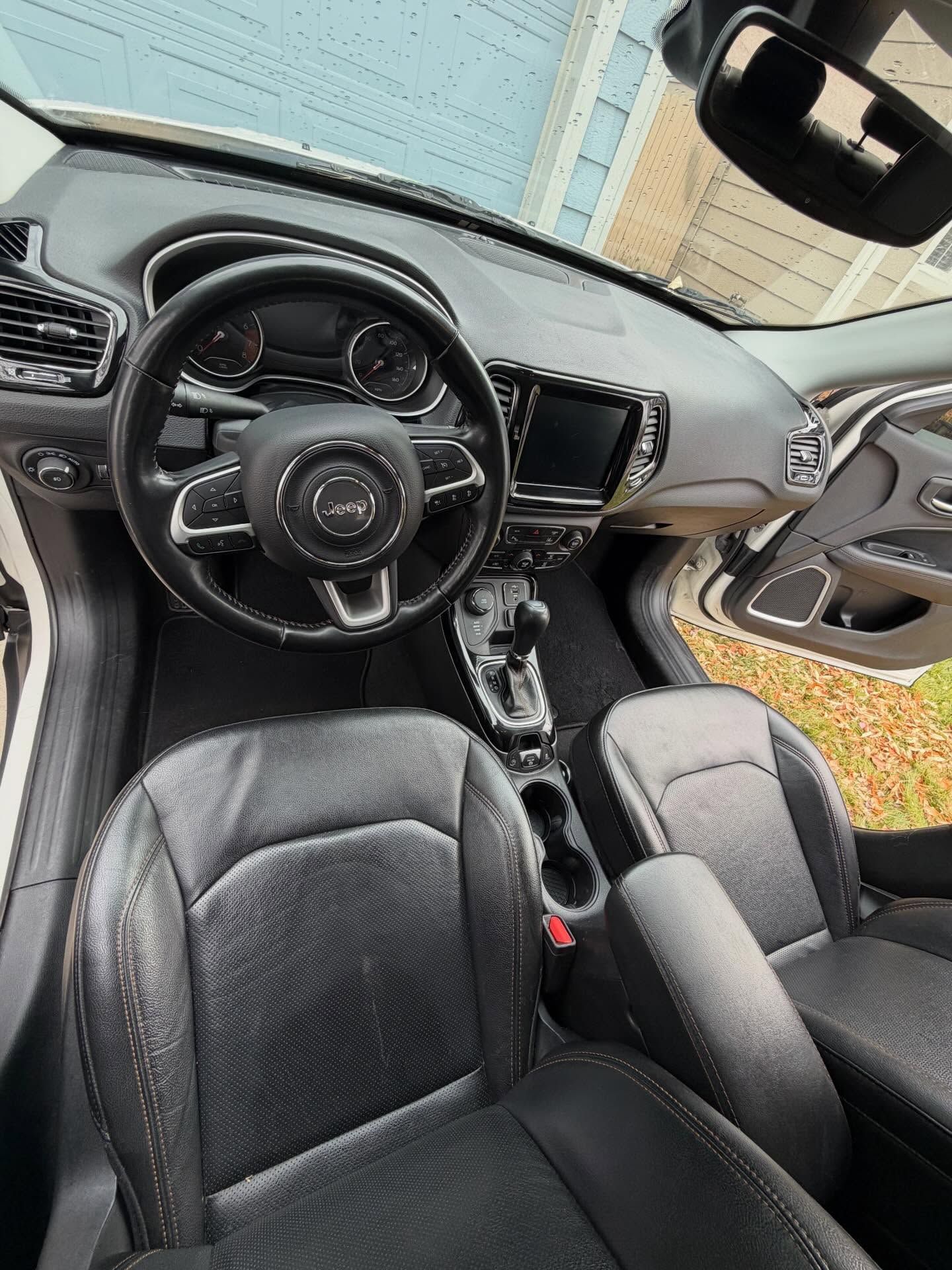 Interior of a black Jeep Compass SUV: black leather seats, dashboard, steering wheel with Jeep logo.