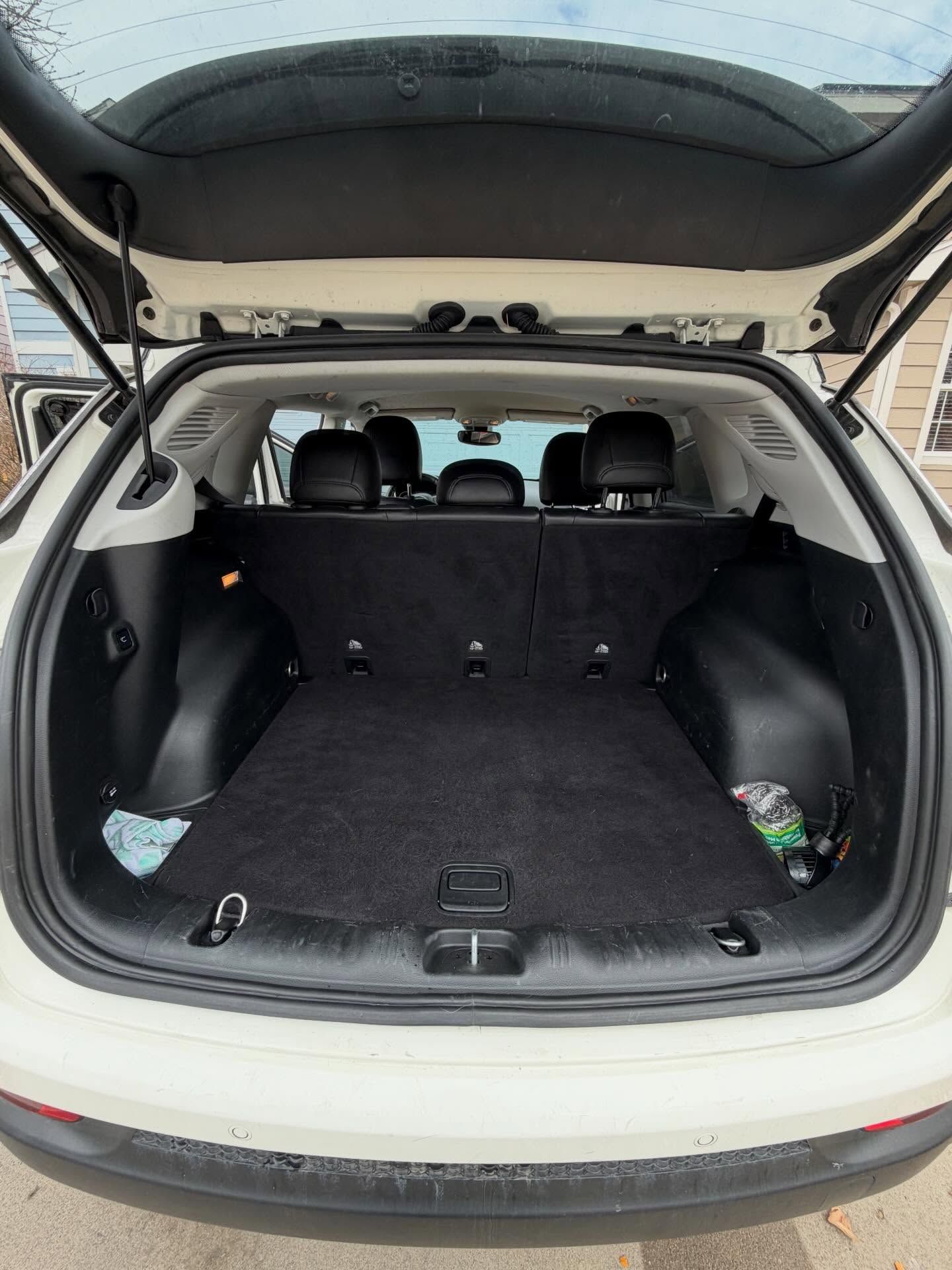 Open white SUV trunk, black carpet, rear seats visible, groceries on right, outdoors.