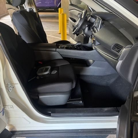 Interior view of a white car with black seats; door open. Steering wheel, dashboard, and center console visible.