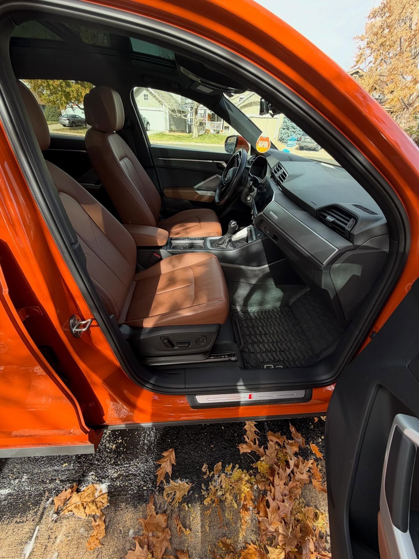 Orange car interior with brown leather seats and black accents. Door open, revealing interior.