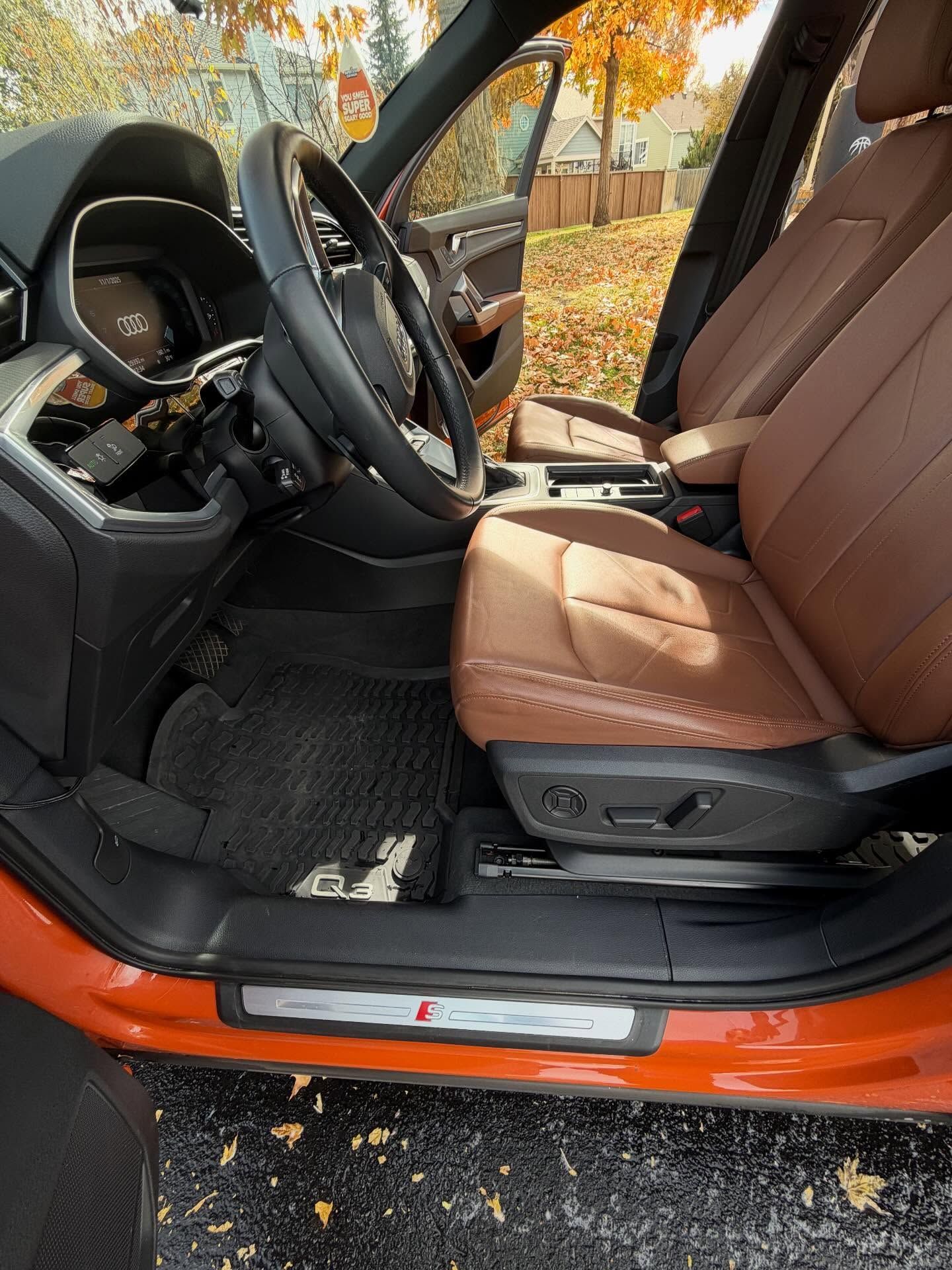 Interior of an orange Audi with brown leather seats and a black steering wheel. Door is open.