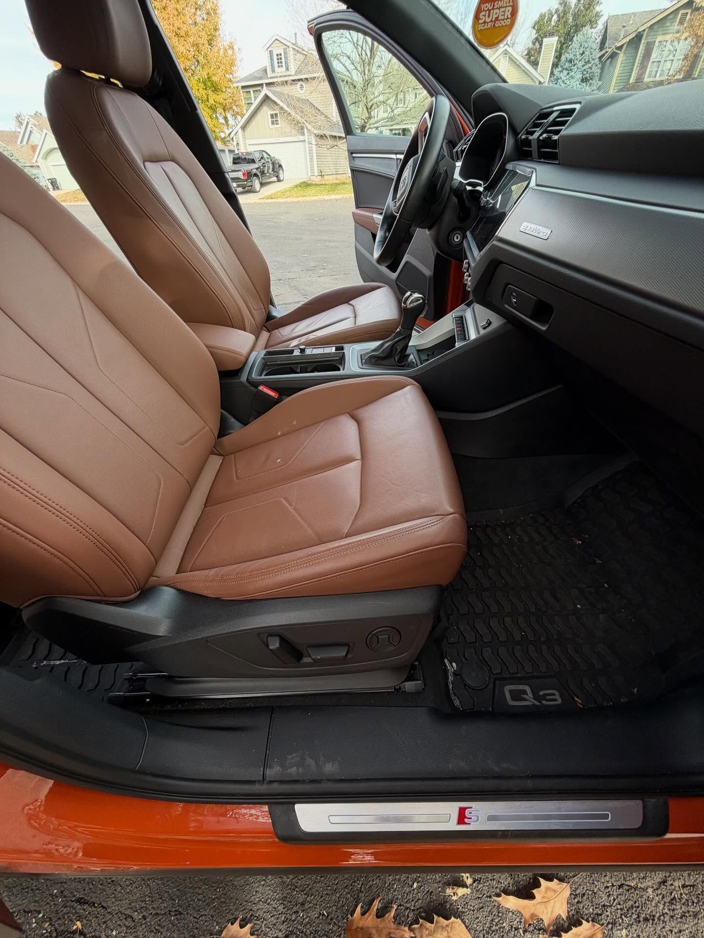 Interior of an Audi Q3 with brown leather seats and a black floor mat, door frame displays 