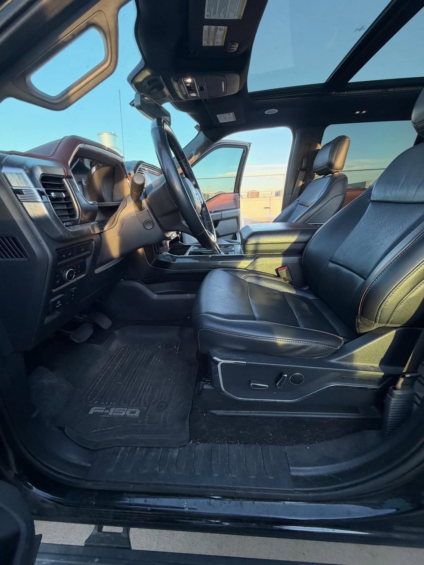 Interior of a black Ford F-150 truck with black leather seats, a panoramic sunroof, and a partially open driver-side door.