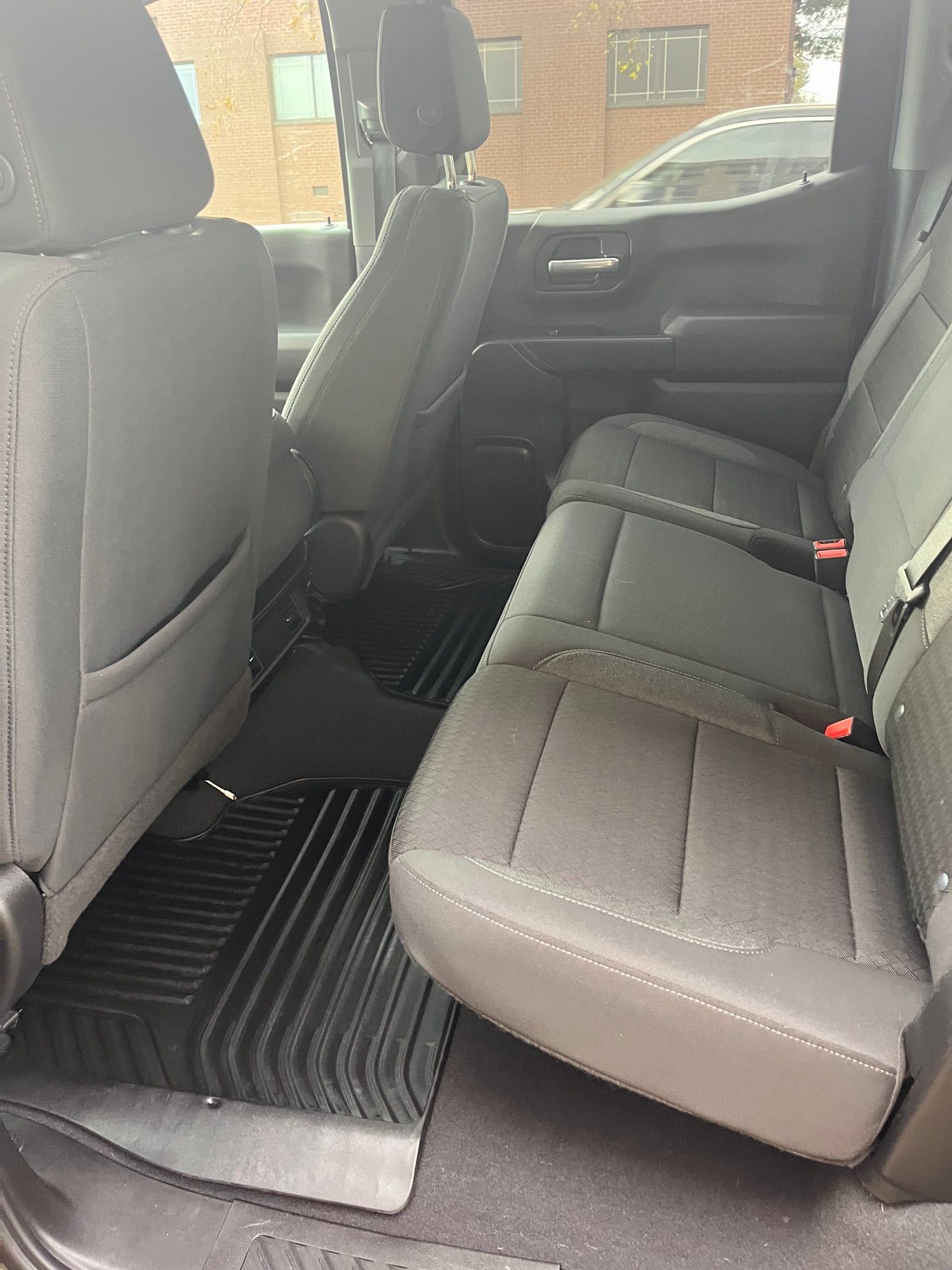 Interior view of a pickup truck's back seat with gray fabric seats, black floor mats, and a window.